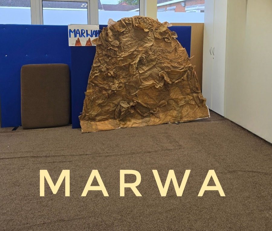 A second hand built rocky hill against a blue classroom wall, with brown floor covering laid out in front